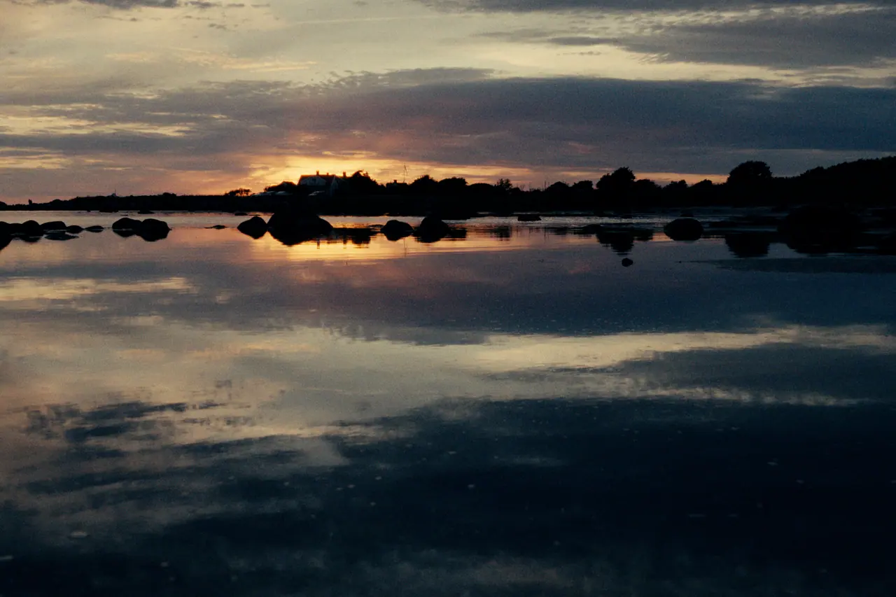 Sunset reflected in still, shallow water between dark rocks